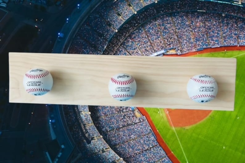May include: A wooden baseball display shelf with three baseballs. Each baseball is white with red stitching and the words "OFFICIAL LEAGUE" printed on it. The shelf is made of light-colored wood.