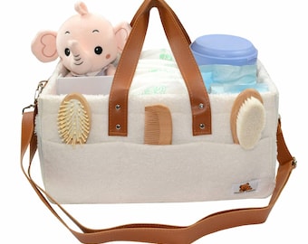 May include: White diaper bag with brown leather handles and a shoulder strap. The bag is filled with baby supplies, including diapers, wipes, a comb, a brush, a stuffed elephant, and a container of lotion.