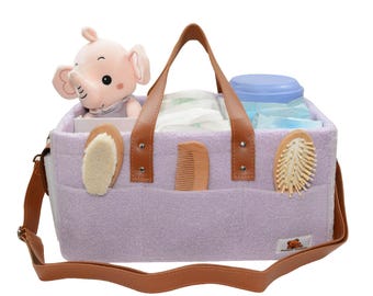 May include: A lavender diaper bag with brown leather handles and a shoulder strap. The bag is filled with baby items, including a stuffed elephant, a comb, a brush, and a container of wipes.