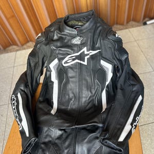 Op de afbeelding: Zwart en wit leren motorracepak met een wit Alpinestars-logo op de borst.