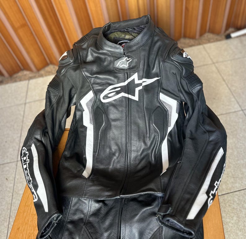 Op de afbeelding: Zwart en wit leren motorracepak met een wit Alpinestars-logo op de borst.