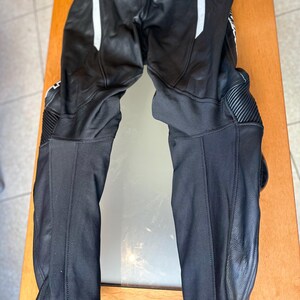 Op de afbeelding: Zwarte leren motorbroek met witte accenten en kniebeschermers.