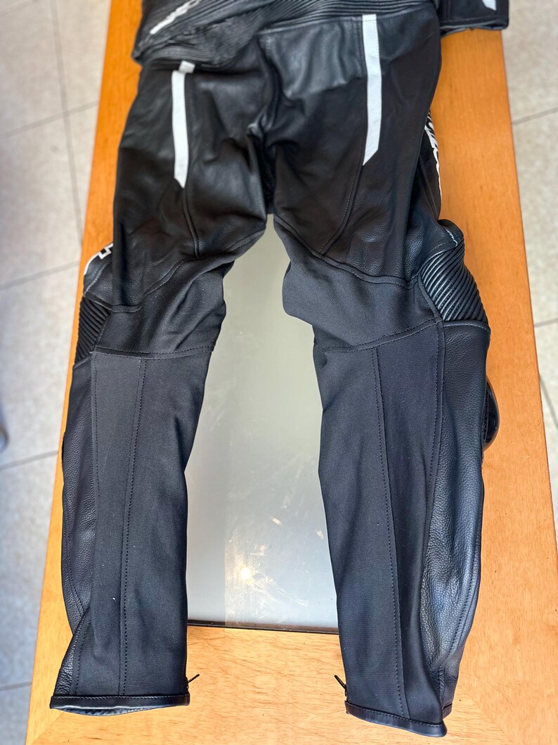Op de afbeelding: Zwarte leren motorbroek met witte accenten en kniebeschermers.