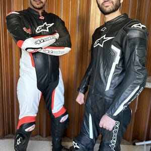 Op de afbeelding: Twee mensen dragen zwarte en witte leren motorpakken met de merknaam "Alpinestars" gedrukt op de pakken.