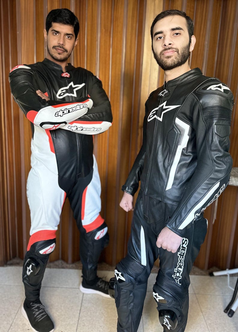 Op de afbeelding: Twee mensen dragen zwarte en witte leren motorpakken met de merknaam "Alpinestars" gedrukt op de pakken.