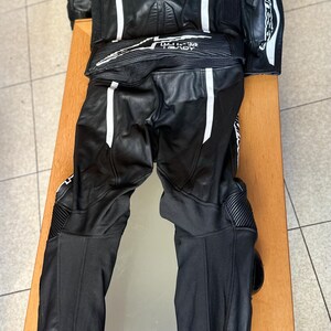 Op de afbeelding: Zwart leren motorracepak met witte accenten en het Alpinestars-logo.