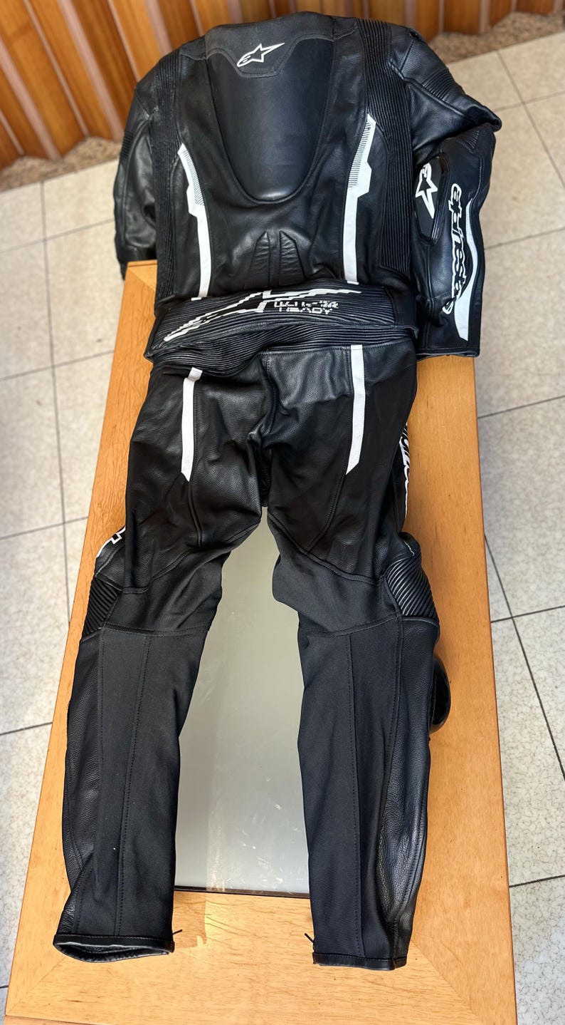Op de afbeelding: Zwart leren motorracepak met witte accenten en het Alpinestars-logo.