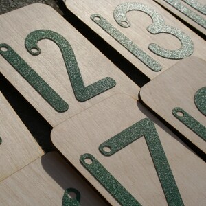 May include: A set of wooden number tiles with green glitter numbers. The numbers are 1, 2, 3, 7, and 8.