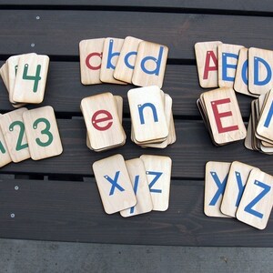 May include: Wooden alphabet and number tiles with blue, red, and green painted letters and numbers. The tiles are arranged in groups of letters and numbers.