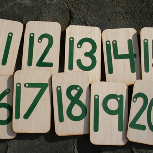 May include: Set of ten wooden number tiles with green numbers from 11 to 20. Each tile has a hole in the top corner.