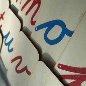 May include: Close-up of wooden alphabet letter tiles with red and blue painted letters. The letters are cursive and include the letters 'm', 'u', and 'o'.