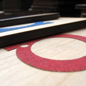 May include: Close-up of a wooden surface with a red circle cutout. The circle is outlined with a red, textured material.