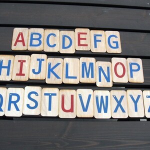 May include: Wooden alphabet blocks with blue and red painted letters. The letters are arranged in alphabetical order from A to Z.
