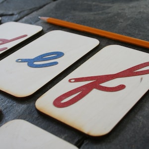 May include: Close-up of five wooden cards with cursive letters 'a', 'd', 'e', 'f' and 'g' in red and blue.