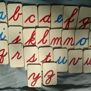 May include: A set of alphabet flashcards with cursive letters in red and blue on white wooden cards. The letters are arranged in alphabetical order.