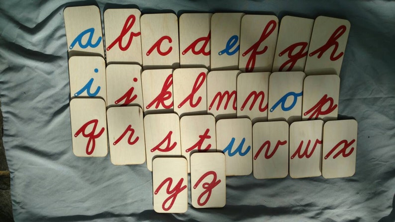 May include: A set of alphabet flashcards with cursive letters in red and blue on white wooden cards. The letters are arranged in alphabetical order.