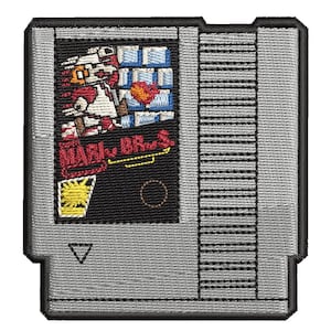 Puede incluir: Parche bordado con un diseño de cartucho de videojuego retro. El parche muestra ilustraciones pixeladas de un personaje con el texto "MARI. BROS." y un icono de sol amarillo. El cartucho tiene un fondo gris con un borde negro.