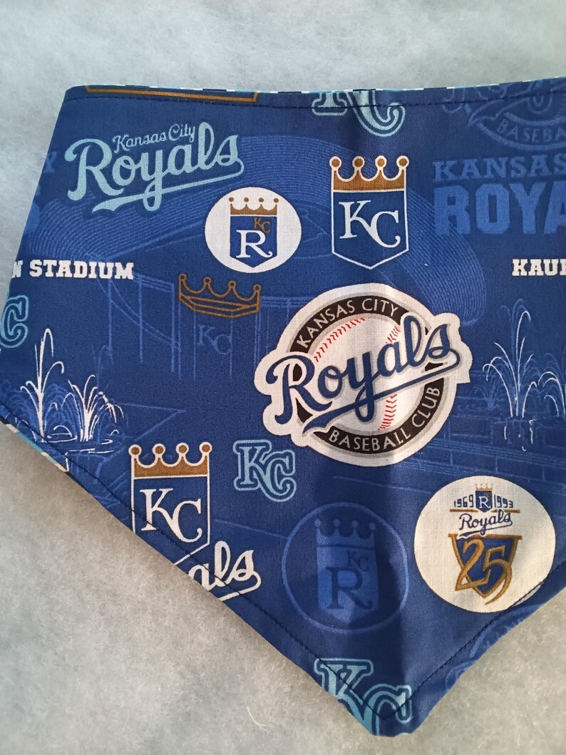 K&ouml;nnte beinhalten: Blau-wei&szlig;es Kansas City Royals Baseball-Team-Bandana. Das Bandana zeigt das Logo des Teams, die Worte "Kansas City Royals" und andere teambezogene Grafiken. Das Bandana ist aus einem weichen Stoff gefertigt.