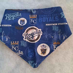 K&ouml;nnte beinhalten: Blau-wei&szlig;es Haustier-Bandana mit dem Logo und Text der Baseballmannschaft Kansas City Royals. Das Bandana hat ein sich wiederholendes Muster aus Logos, Kronen und den W&ouml;rtern "Royals" und "Kauffman Stadium".