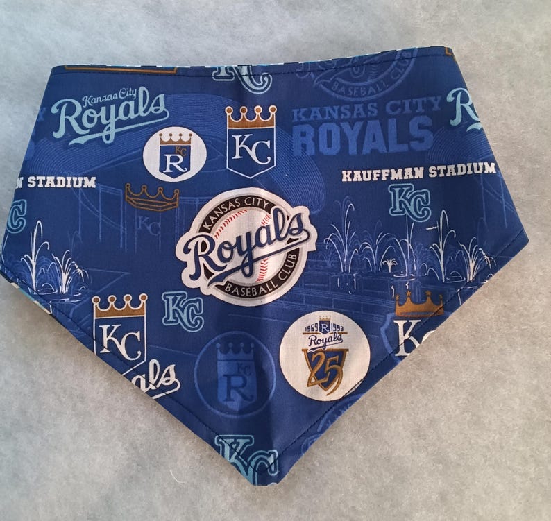 K&ouml;nnte beinhalten: Blau-wei&szlig;es Haustier-Bandana mit dem Logo und Text der Baseballmannschaft Kansas City Royals. Das Bandana hat ein sich wiederholendes Muster aus Logos, Kronen und den W&ouml;rtern "Royals" und "Kauffman Stadium".