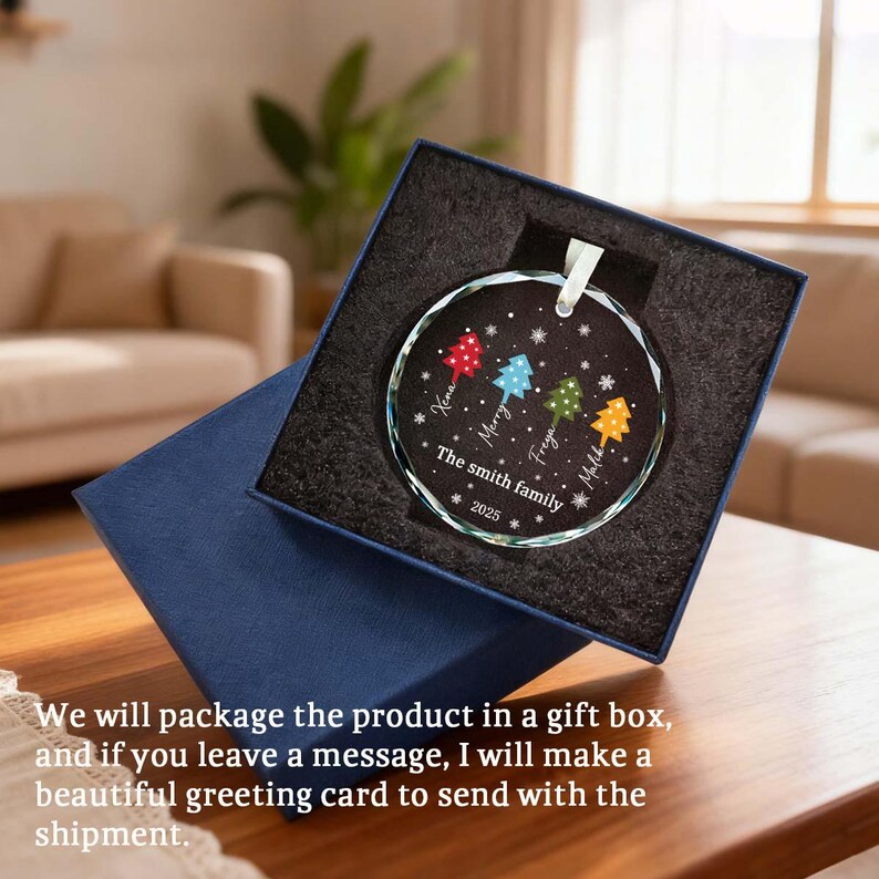 May include: A clear glass Christmas bauble with a white ribbon, presented in a blue gift box. The bauble features colourful Christmas trees and the text "The Smith family 2025".