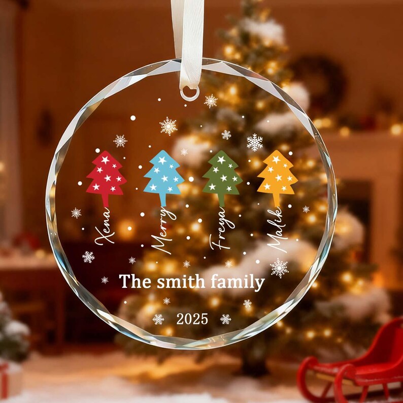 May include: A clear, round Christmas bauble with a white ribbon. The bauble features four colourful Christmas trees and the names Xena, Merry, Freya, and Malik. The text "The Smith family 2025" is also displayed.