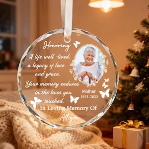 May include: A clear, round memorial ornament with a photo of a woman, surrounded by text and butterfly graphics. The text reads "Honoring, A life well-lived, a legacy of love and grace. Your memory endures in the lives you touched. In Loving Memory Of Allegra."