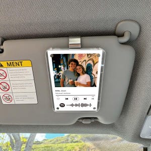 Peut inclure: Un accessoire de pare-soleil de voiture en acrylique transparent avec une photo d'un couple et une interface de lecteur de musique Spotify. La chanson est "Billie Jean" de Michael Jackson. Le pare-soleil est gris.