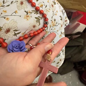 Könnte beinhalten: Eine rote Perlenkette mit einem lila Blumenanhänger und einem rosafarbenen Kreuzanhänger.