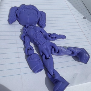 May include: A purple articulated doll with a detailed design. The doll has a head with pigtails, a detailed torso, and articulated limbs. It is holding a small bucket. The doll is made of plastic.