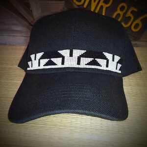 May include: A black baseball cap with a white and black beaded design across the front. The design features geometric shapes.