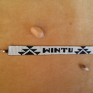 May include: Black and white beaded bracelet with the word "INTUIT" spelled out in black beads. The bracelet has a silver clasp and a gold accent.
