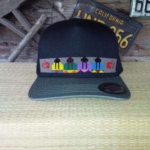 May include: A black baseball cap with a gray brim. The cap features a colorful beaded design across the front with red, yellow, green, purple, and blue accents. A California license plate is visible in the background.