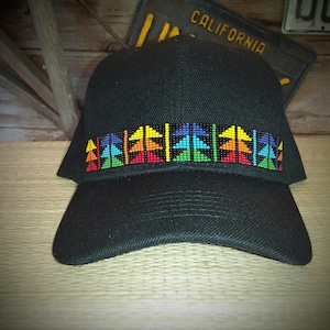 May include: Black baseball cap with a colorful geometric design across the front. The design features triangles in shades of red, orange, yellow, green, and blue. The cap is made of a sturdy material and has a curved brim.