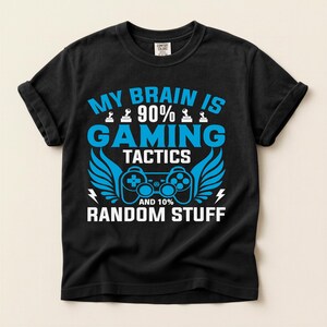 以下が含まれることがあります： 「MY BRAIN IS 90% GAMING TACTICS AND 10% RANDOM STUFF」というテキストが青と白でプリントされた黒いTシャツ。デザインにはゲームコントローラー、翼、稲妻が含まれています。Tシャツはクルーネックで半袖です。