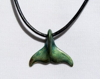 May include: A green and gold whale tail pendant necklace on a black leather cord.