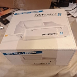 May include: A white Poweroll 2 electric cigarette machine in its original packaging. The box is white with blue text that reads "KING SIZE & 100MM" and "POWERROLL 2 ELECTRIC CIGARETTE MACHINES". A cigarette is visible.