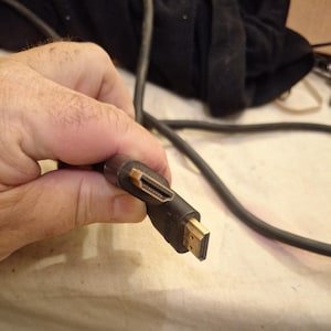 May include: A black HDMI cable featuring two gold-plated connectors at the end of the cord. The cable is flexible and round, with the brand name Vizio embossed on the plastic housing of the connector head, showing a standard digital interface.