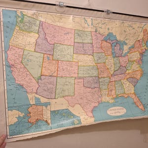 Könnte beinhalten: Eine Wandkarte der Vereinigten Staaten im Vintage-Stil mit pastellfarbenen Bundesstaaten, schwarzen Textbeschriftungen für Städte und Regionen sowie Kartenausschnitten von Alaska und Hawaii. Die Karte hat einen Gitterrand und den Text United States.