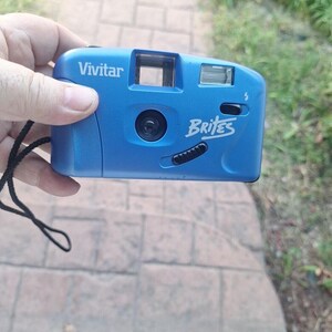 May include: A blue Vivitar Brite's point and shoot camera with a black strap.