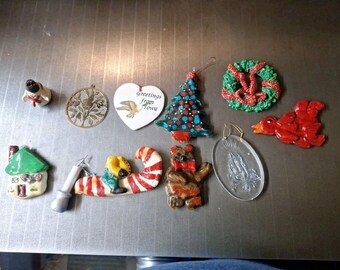May include: A collection of handmade Christmas ornaments, including a snowman, a bird in a wreath, a candy cane, a house, a tree, a bear, a bird, a wreath, and a religious figure. The ornaments are made of various materials, including clay, glass, and metal.