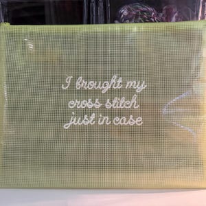 May include: A light green, mesh-like zippered pouch with the embroidered text "I brought my cross stitch just in case." The pouch is rectangular and appears to be made of a durable, semi-transparent material, ideal for storing craft supplies.