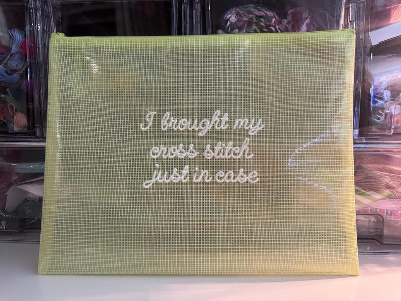 May include: A light green, mesh-like zippered pouch with the embroidered text "I brought my cross stitch just in case." The pouch is rectangular and appears to be made of a durable, semi-transparent material, ideal for storing craft supplies.