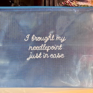 May include: A blue zippered pouch with a grid pattern and the embroidered text "I brought my needlepoint just in case." The pouch has a blue zipper and pull tab. Ideal for storing craft supplies.