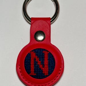 May include: Red leather keychain with a silver ring and a round blue and red embroidered patch with the letter "N" in the center.