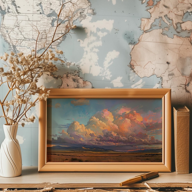 May include: A framed landscape painting depicting a dramatic, colorful sunset over a field. The sky is filled with large, fluffy clouds in shades of pink, orange, and purple. The field is a muted green, and the horizon is a dark blue.