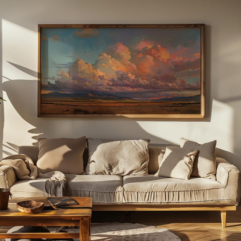 May include: A framed landscape painting depicting a vast, golden field with a dramatic, pink-hued cloud formation in the sky. The painting is hanging on a white wall above a beige sofa with pillows.