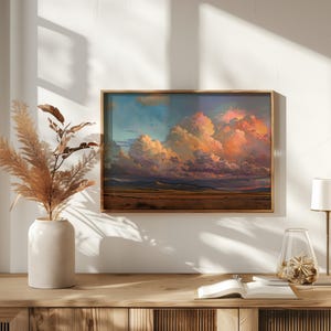 May include: A framed landscape painting depicting a dramatic sunset over a field with large, fluffy clouds in shades of pink, orange, and purple.