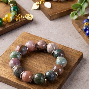 Może przedstawiać: Bransoletka wykonana z wielokolorowych koralików agatowych z srebrnymi akcentami. Bransoletka jest prezentowana na drewnianym stojaku.