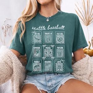 May include: Teal green t-shirt with the words "Seattle Baseball" in white script. Below the text are nine white illustrations of baseball-related items, including a hot dog, popcorn, and a baseball glove.